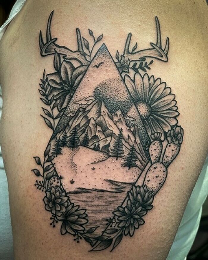 Nature tattoo featuring mountains, trees, and flowers with antlers, symbolizing the human-Earth bond.