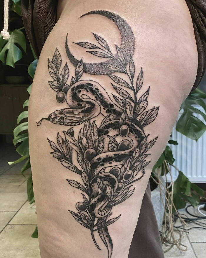 Nature tattoo featuring a snake entwined with leaves and berries, with a crescent moon in the background.