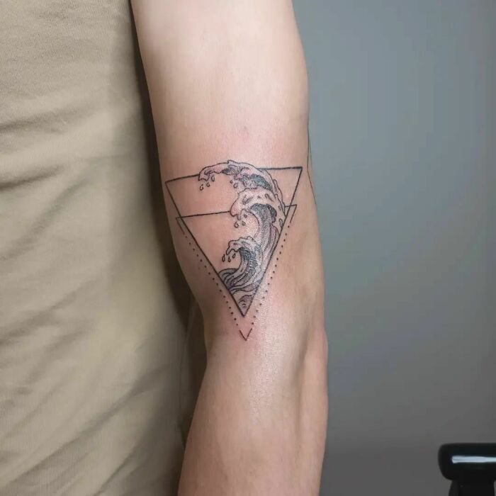 Wave tattoo in triangle on forearm, celebrating human-earth bond with nature theme.