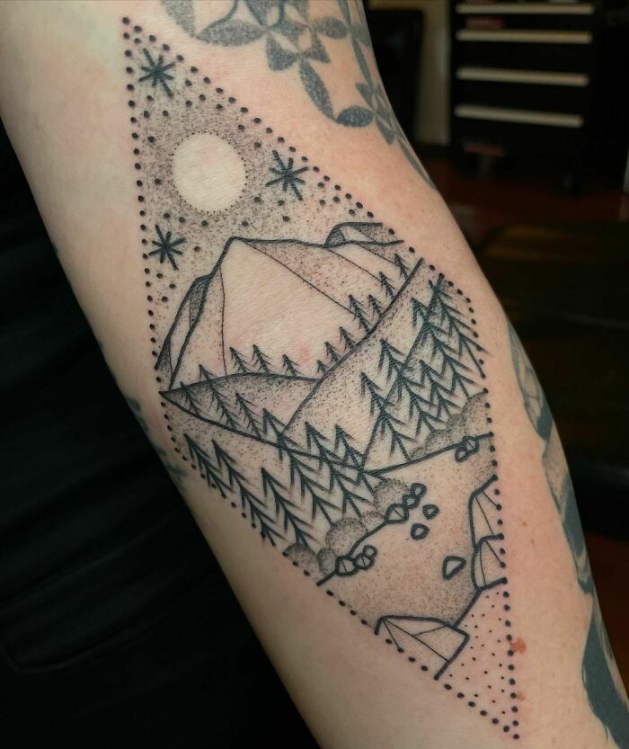 Nature tattoo depicting mountains, trees, and a sun in geometric design on an arm.