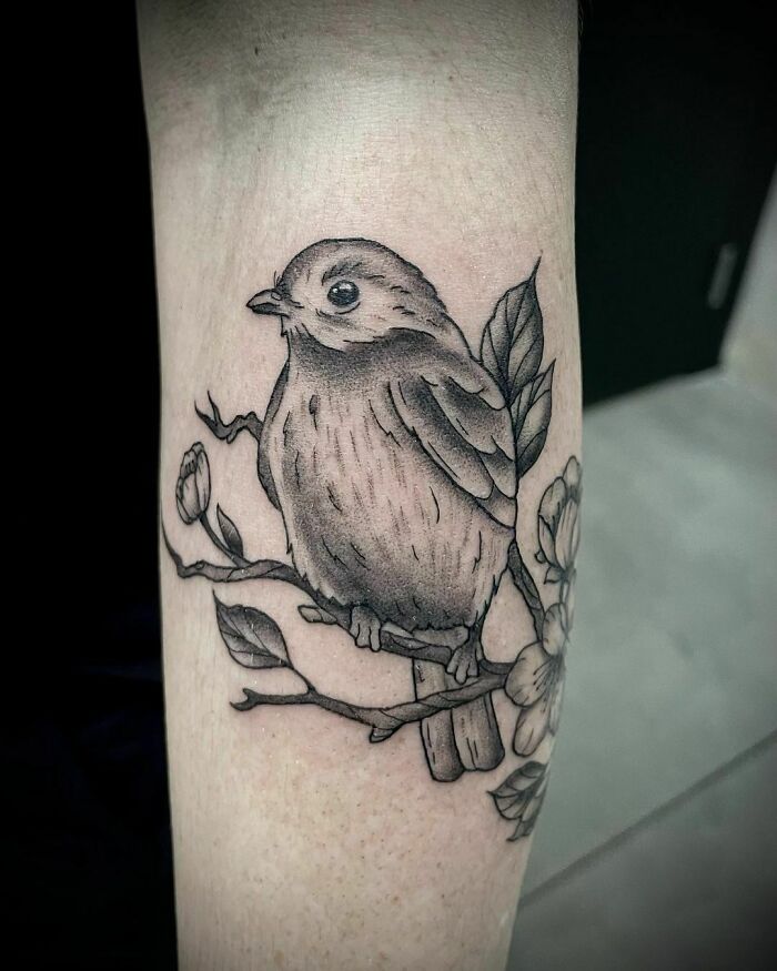 Nature tattoo of a bird perched on a branch with leaves and flowers, symbolizing the wonders of Mother Earth.
