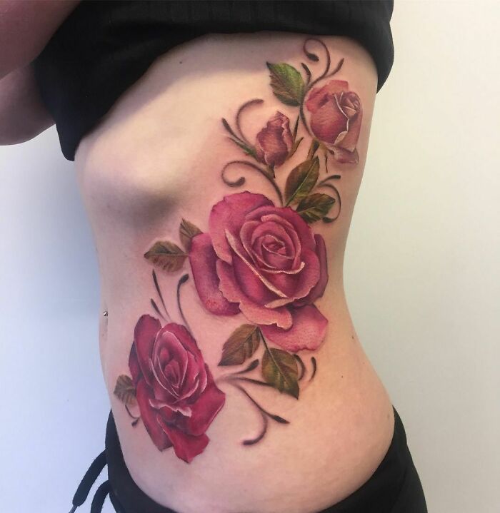 Floral nature tattoo on side of a person's torso, featuring detailed pink roses and green leaves.