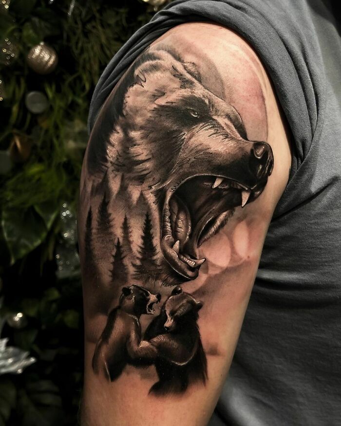 Bear tattoo on arm featuring a roaring bear and trees, representing nature and the human-earth connection.