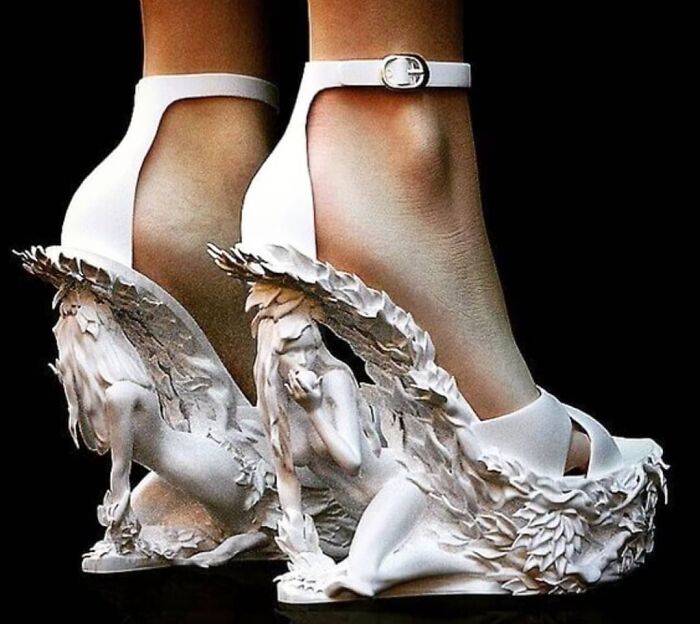 Weird shoes featuring intricate white sculptures of a seated figure with leaf detailing on high heels.