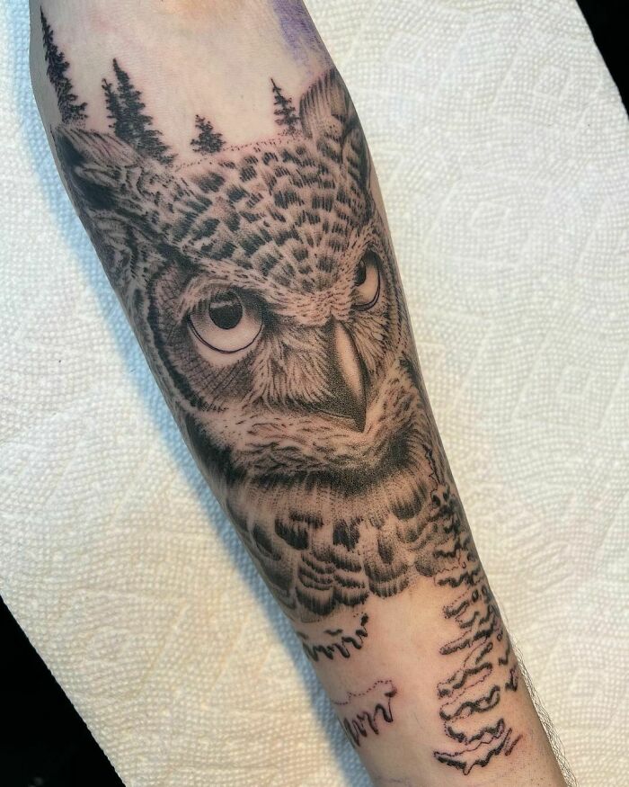 Realistic owl tattoo on forearm with forest design, showcasing nature tattoos for those with a wild side.