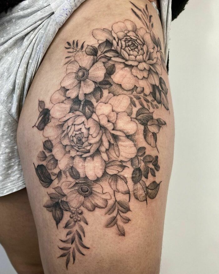 Floral nature tattoo on upper thigh, showcasing detailed flower and leaf design.