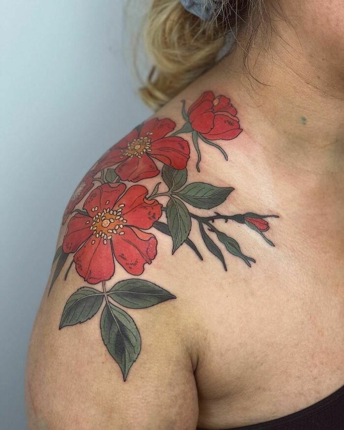 Floral nature tattoo with red flowers on a shoulder, celebrating the human-earth bond.