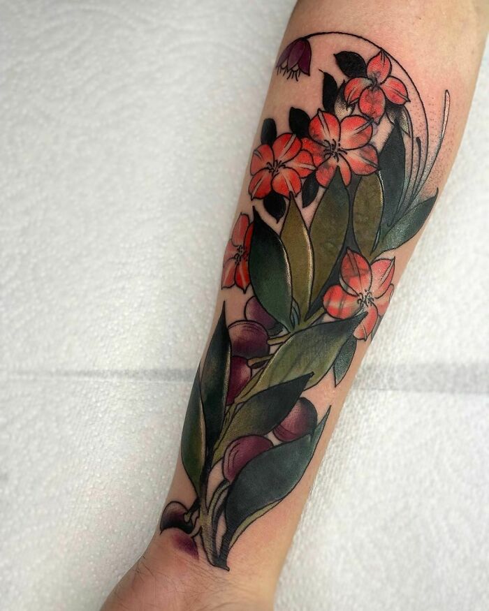 Colorful nature tattoo featuring vibrant flowers and green leaves on a forearm.