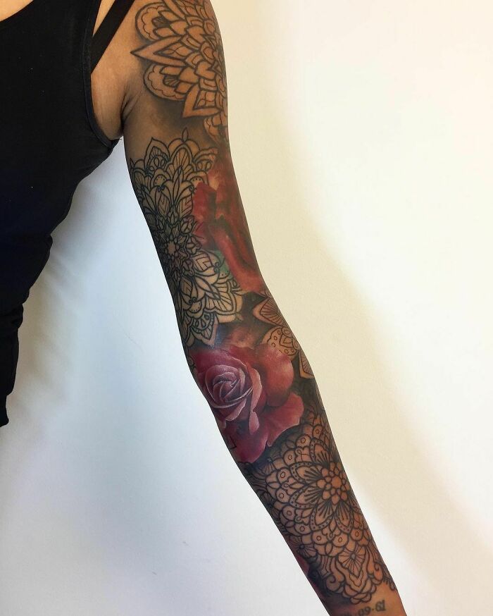 Intricate sleeve with floral designs, featuring a red rose, showcasing nature tattoos on an arm.
