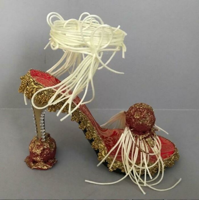 Weird shoe with noodle-like design, red and gold details, and decorated stiletto heel.