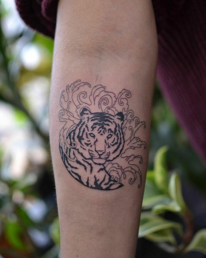 Tiger nature tattoo design on forearm, surrounded by decorative waves, symbolizing the human-earth bond.