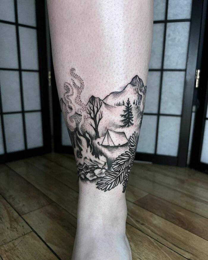 Nature tattoos featuring mountains, trees, and a tent, symbolizing the beauty of the outdoors on a person's leg.