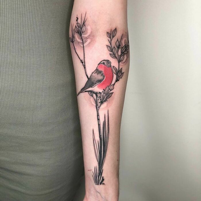 Arm with a nature tattoo featuring a colorful bird perched on a branch.