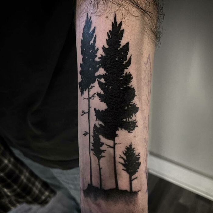 Forearm nature tattoo featuring silhouettes of tall pine trees, designed for those with a wild side.