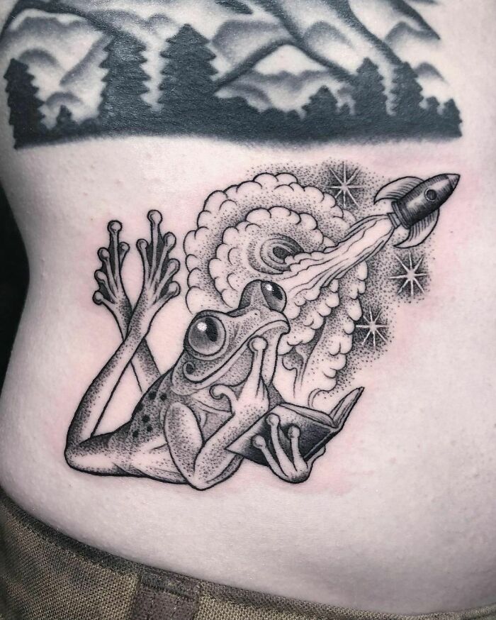 Frog nature tattoo with rocket, celebrating human-earth bond, inked on skin with mountain silhouette background.