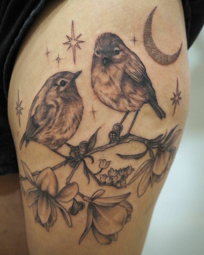 Nature tattoo featuring birds on a branch with flowers and celestial elements.