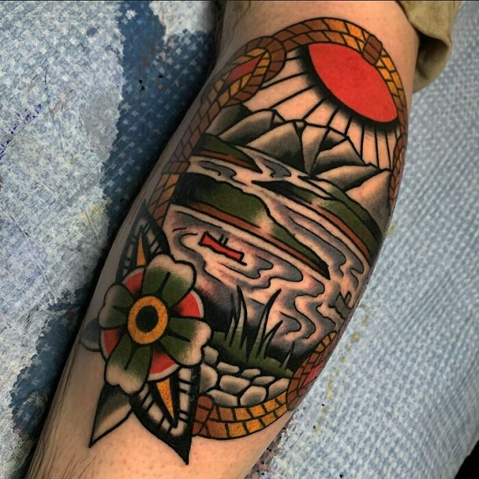 Colorful nature tattoo featuring mountains, a red sun, and a flower on a person's arm.