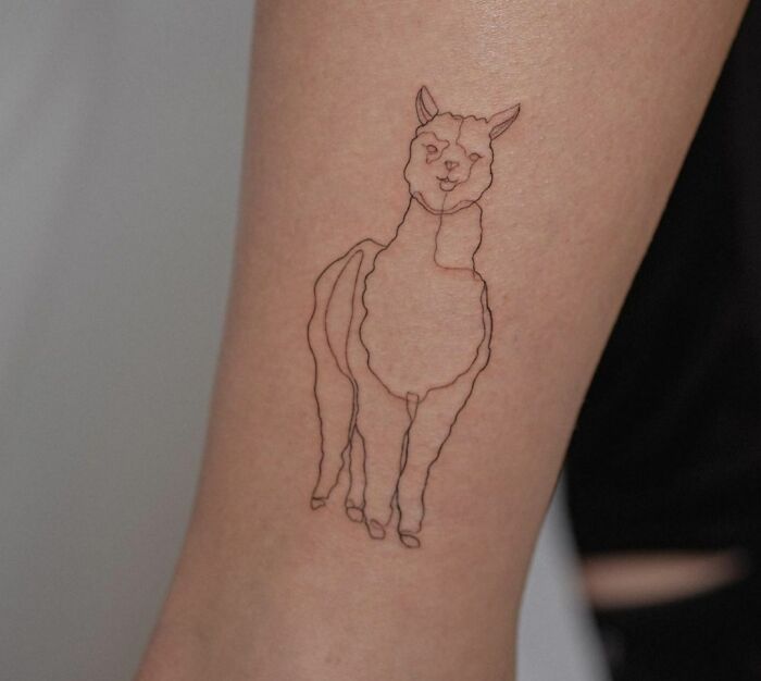 Single-line tattoo of a smiling llama on a person's forearm.