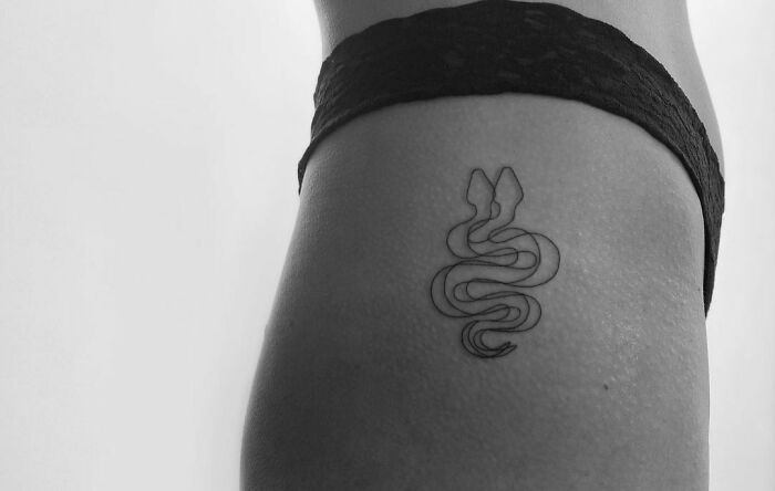 Single-line tattoo of a snake on a person's side, showcasing minimalist tattoo design.