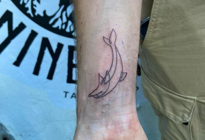 A delicate single-line shark tattoo on a person's forearm, showcasing minimalist design and precision.