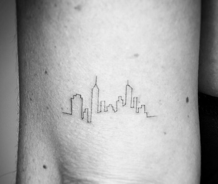 Single-line tattoo of a city skyline on skin.