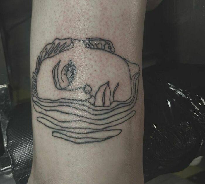 Single-line tattoo of a woman's face partially submerged in water, with flowing lines on a person's skin.