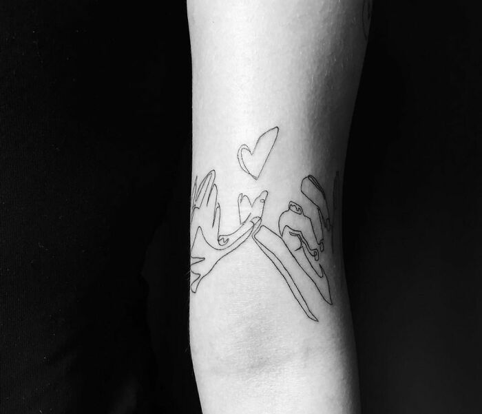 Single-line tattoo of two hands and a heart on an arm.