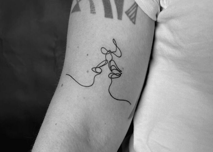 Single-line tattoo of abstract faces on upper arm.