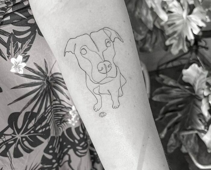 Tattoo of a dog drawn in a single line on a person's arm, showcasing minimalist tattoo art.
