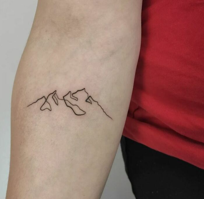Minimalistic single-line tattoo of a mountain range on the forearm, showcasing pure perfection in design.
