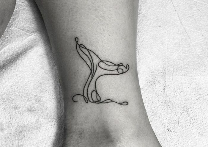 Single-line tattoo of an abstract design on a person's ankle, showcasing minimalist art.