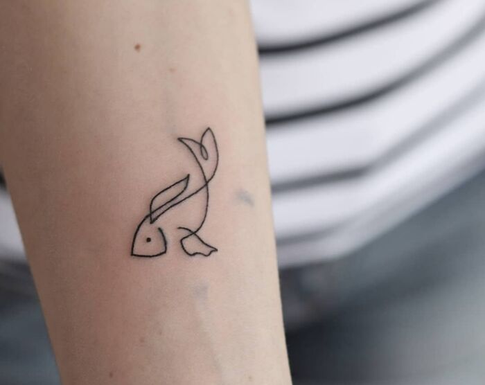Single-line tattoo of a fish on an arm, showcasing minimalist art style.