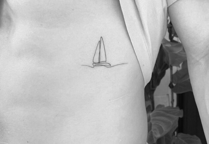 Single-line tattoo of a sailboat on a person's ribcage, displaying minimalist art and pure perfection.