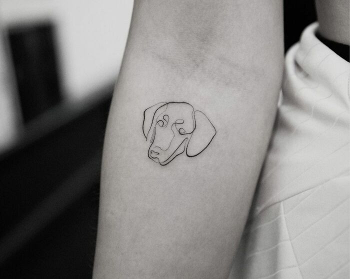Single-line tattoo of a dog's face on a person's arm, showcasing minimalist design.