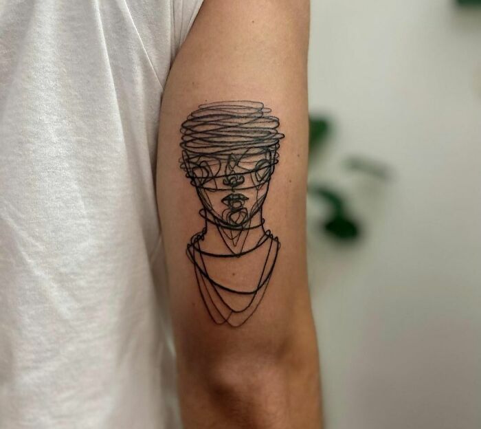 Single-line tattoo on an arm featuring an abstract face design.