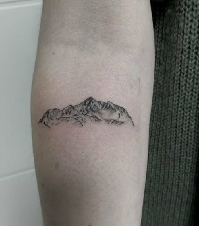Mountain nature tattoo on arm, showcasing wild side through minimalist design.
