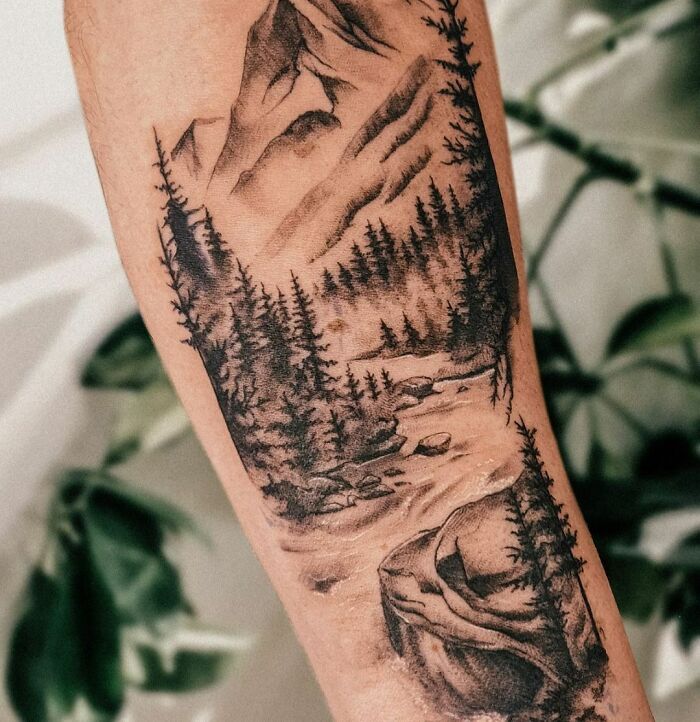 Nature tattoo featuring a detailed mountain landscape with trees and a flowing river.