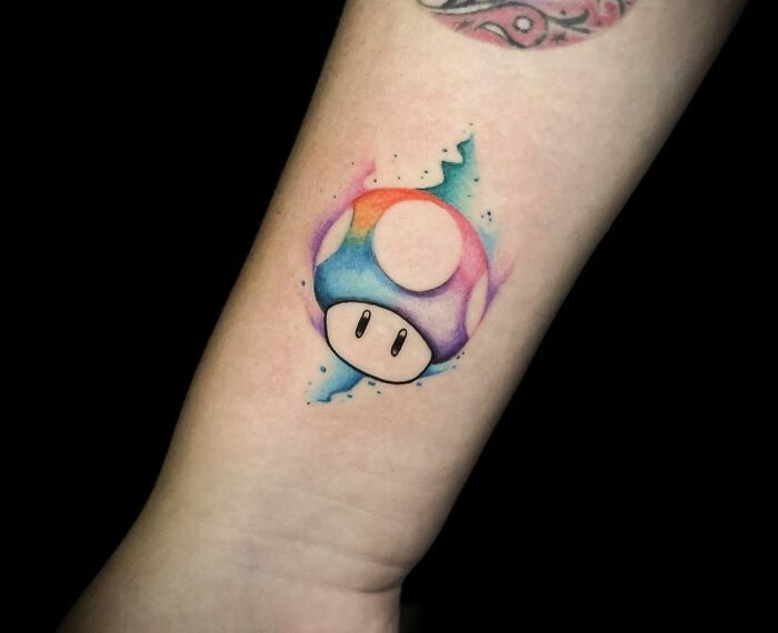 Colorful mushroom watercolor tattoo, blending rainbow hues, on forearm. Ethereal art with vibrant tones.