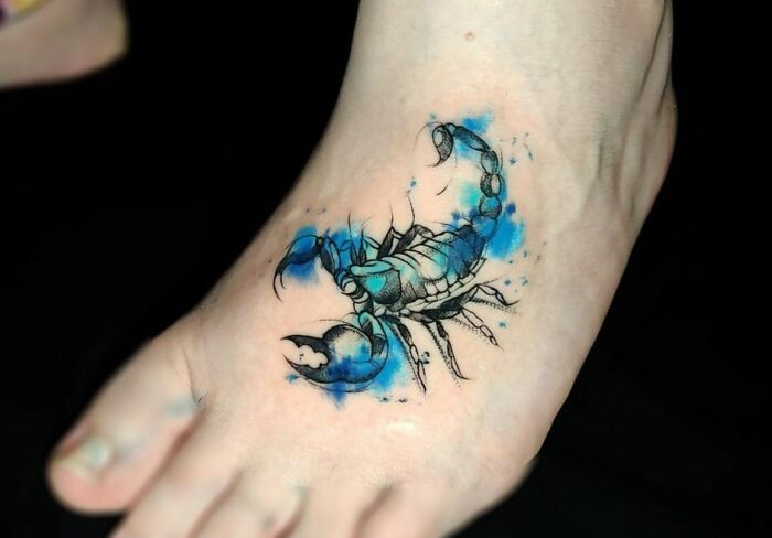 Ethereal watercolor tattoo of a scorpion with blue accents on a foot.