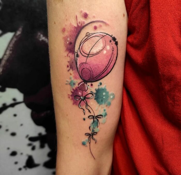 Watercolor tattoo of a balloon with pink and blue splashes, creating an ethereal design on the forearm.
