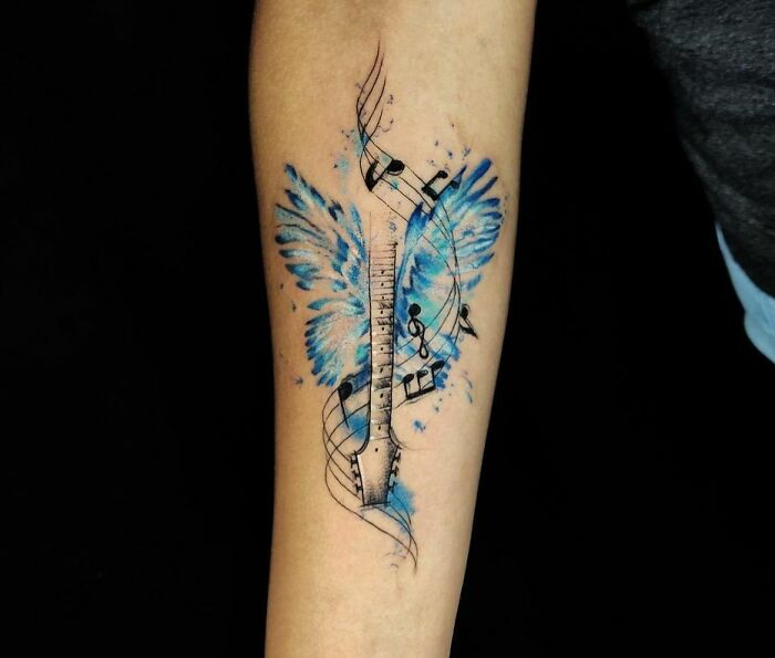 Watercolor tattoo featuring music notes and blue butterfly wings on a forearm.