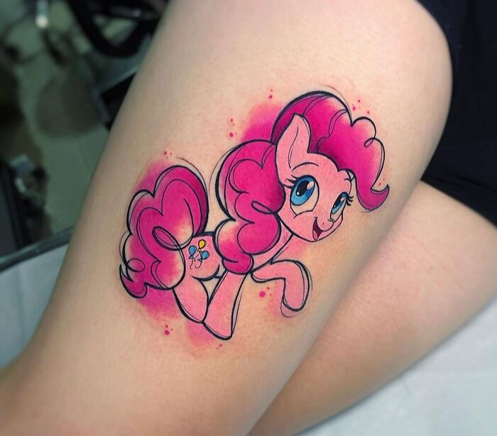 Watercolor tattoo of a pink cartoon pony on a person's leg.