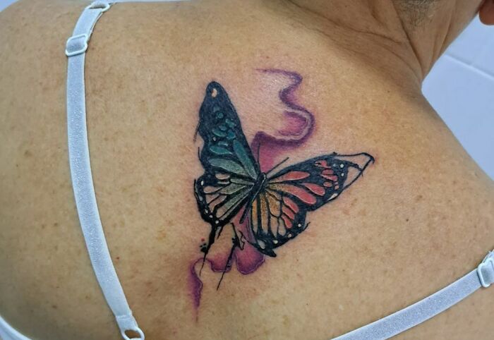Watercolor tattoo of a butterfly with vibrant colors on a person's back in an ethereal design.