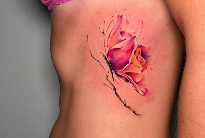 Ethereal watercolor tattoo of a pink rose on a person's side.