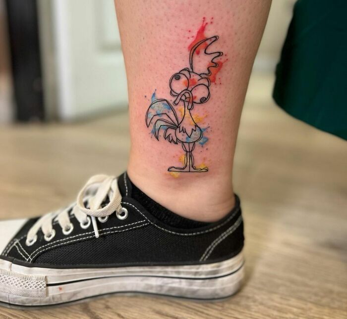 Ethereal watercolor tattoo of a cartoon rooster on a person's leg, near an ankle wearing black sneakers.