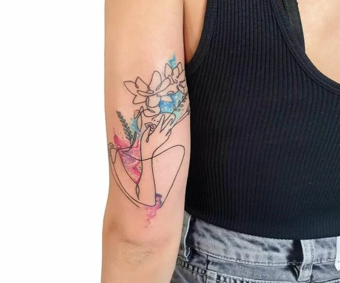 Person wearing a black top with ethereal watercolor tattoo of flowers and abstract line art on their arm.