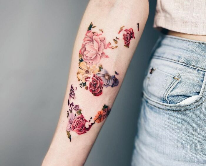 Watercolor tattoo of vibrant flowers on forearm, showcasing ethereal artistry against a neutral background.