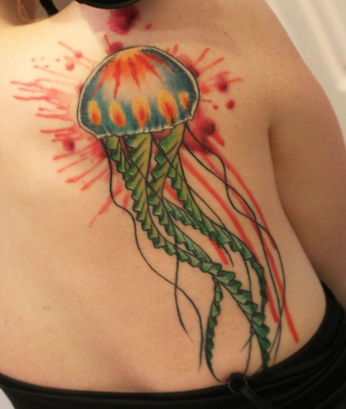 Ethereal watercolor tattoo of a vibrant jellyfish on a person's back, with intricate details and vivid colors.