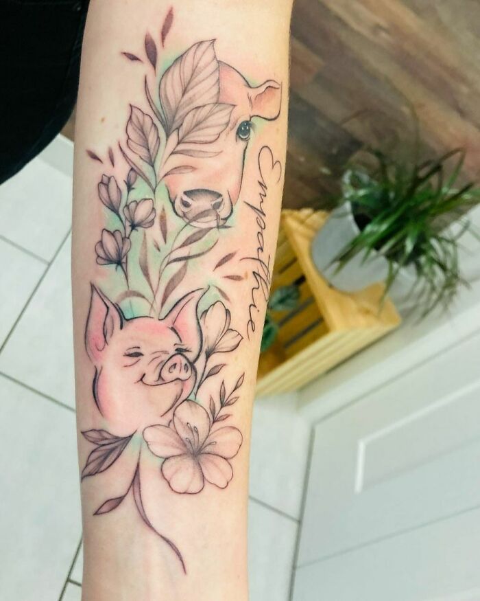 Watercolor tattoo of cow and pig with floral elements on arm, featuring the word "empathie." Ethereal and colorful design.