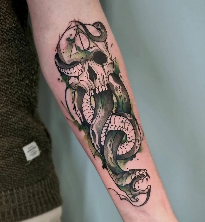 Watercolor tattoo on forearm featuring a skull with snake and ethereal watercolor shading.